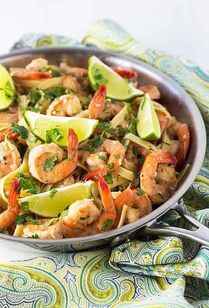 Shrimp and fettuccine topped with lime wedges and cilantro in a skillet. 