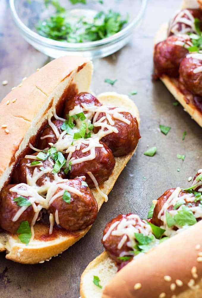 A closeup of a meatball sub topped with shredded mozzarella and parsley.