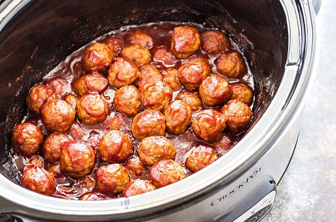 Cooked cranberry meatballs in an oval stainless crock pot.