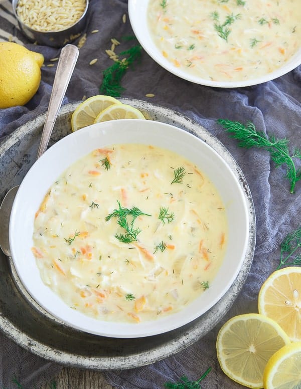 Overhead view of two white bowls of turkey avgolemono soup by sliced lemons.