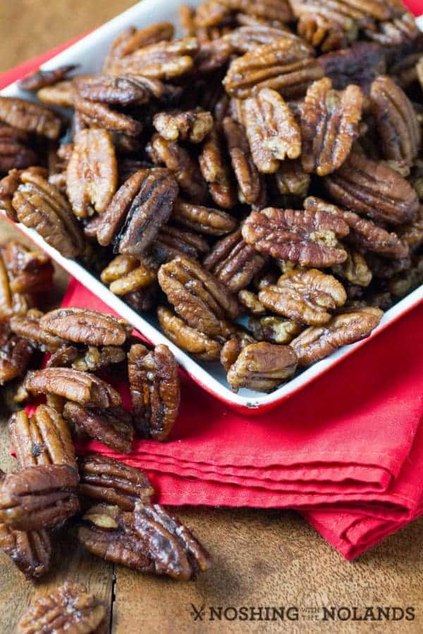 Spiced pecans in a square white bowl on top of a folded red napkin.