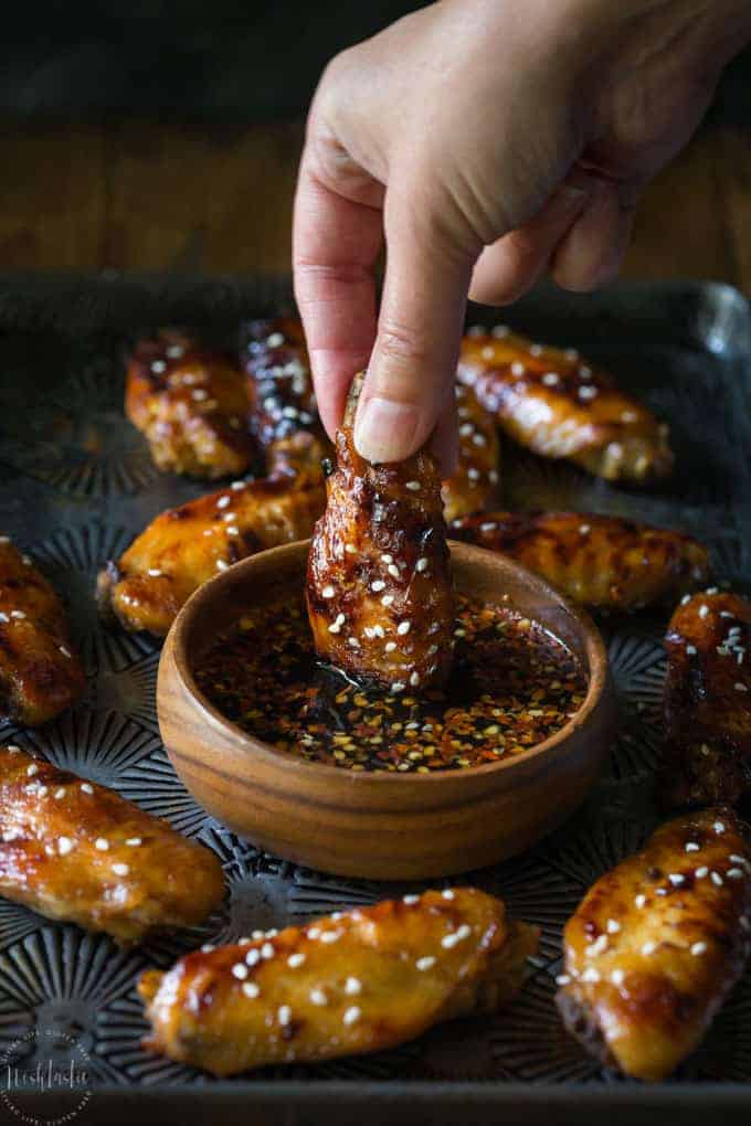 A hand dipping a chicken wing into a wooden bowl of sauce.