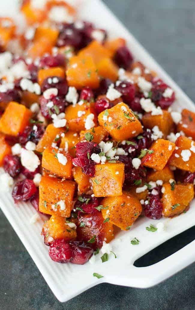 Roasted butternut squash with cranberries and feta cheese in a white dish.