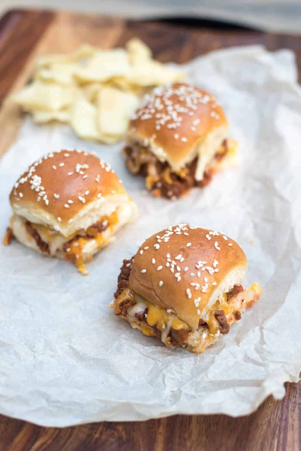 Three sloppy joe sliders on a piece of parchment paper with potato chips.