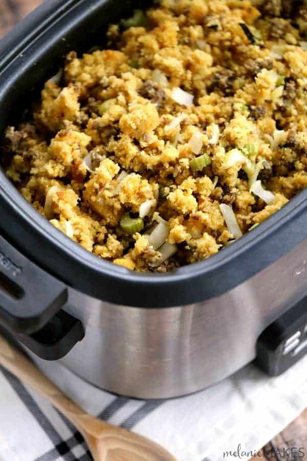 Cornbread and sausage stuffing in a stainless slow cooker by a wooden spoon.