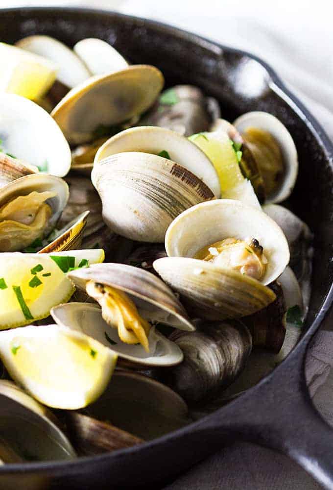 Closeup view of steamed clams in a cast iron skillet.