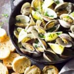 Overhead view of steamed clams in a cast iron skillet by sliced French bread.