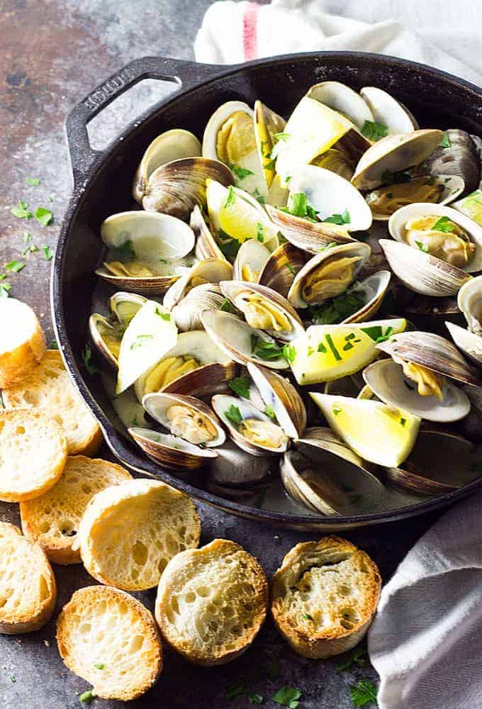 Overhead view of steamed clams in a skillet by sliced French bread.