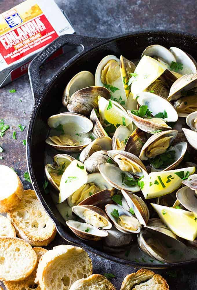 Overhead view of steamed clams in a cast iron skillet by sliced French bread.