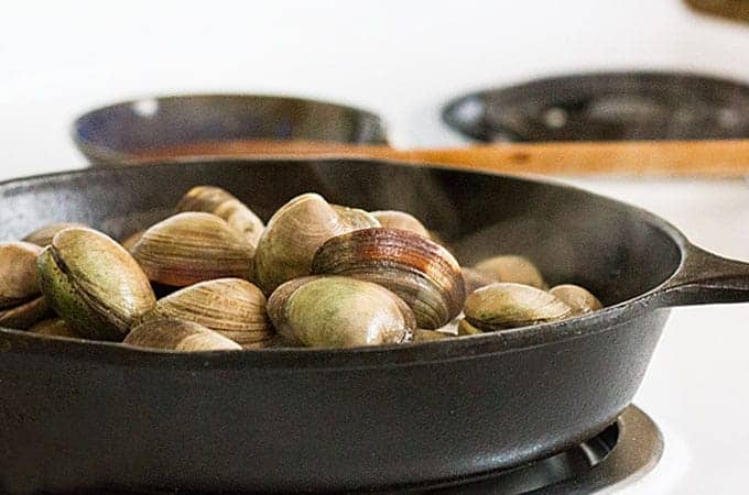Clams in a cast iron skillet on a stove top.