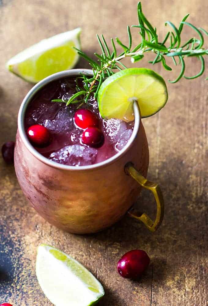 Overhead view of a mule cocktail in a copper mug garnished with cranberries, lime and rosemary.