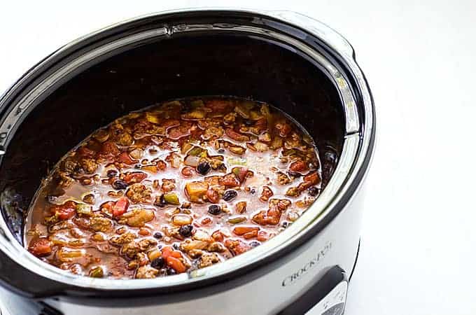 Chili with beef and black beans in an oval stainless slow cooker.