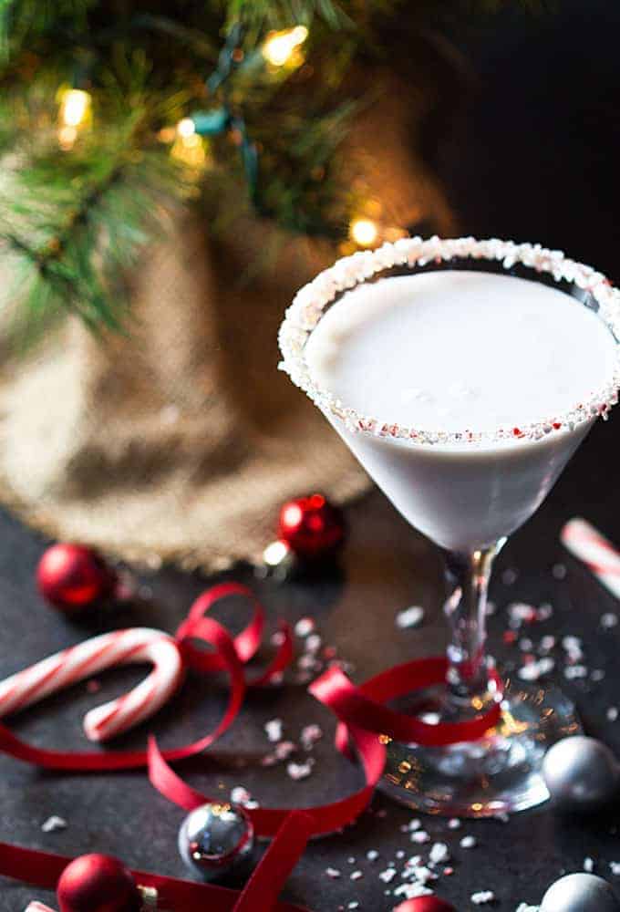 A martini in a glass rimmed with crushed candy canes.  A small holiday tree is in the background.