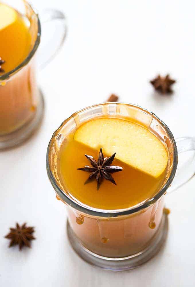 Angled overhead view of a hot toddy with an apple slice and a star anise in a clear mug.