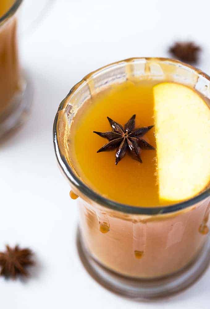 Closeup view of the top of a mug of hot toddy with a caramel rim, sliced apple and a star anise.