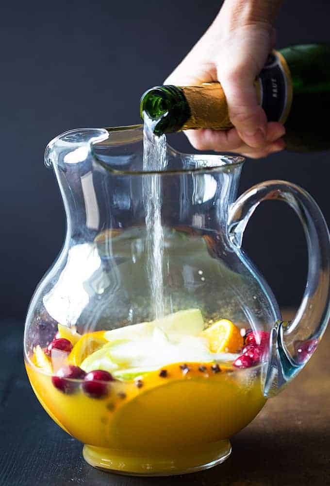 Pouring champagne into a pitcher with orange juice and fruit.