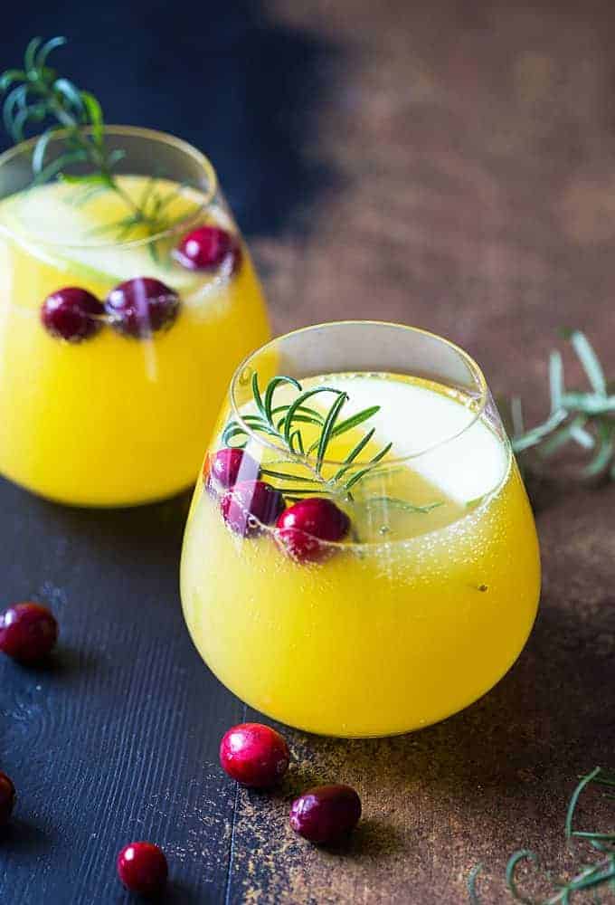 Two glasses of sangria with orange juice and champagne garnished with cranberries and rosemary.