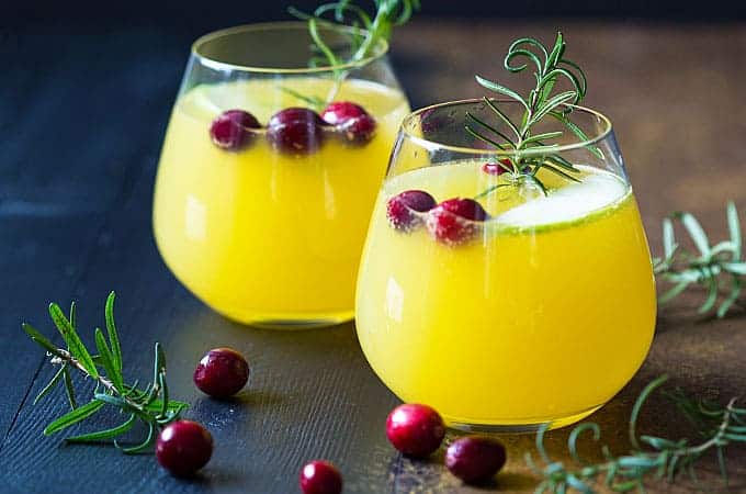 Front view of two glasses of champagne sangria with cranberries and rosemary sprigs.
