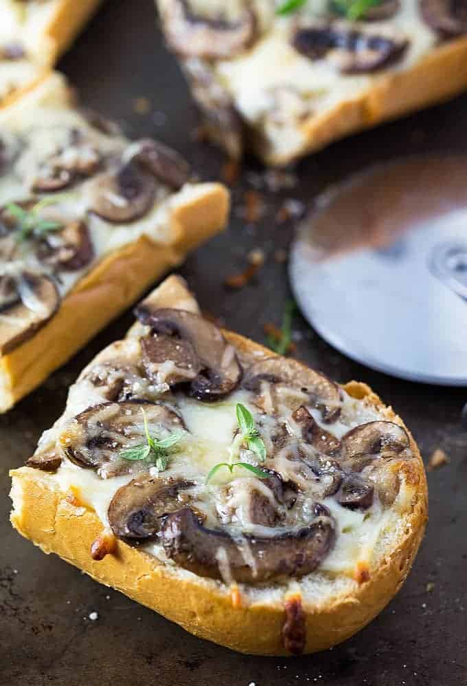 Closeup view of a slice of french bread pizza topped with mushrooms and fresh thyme.