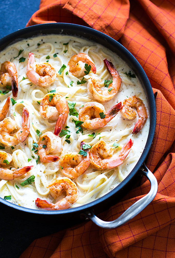 Overhead view of shrimp Alfredo in a skillet by an orange patterned napkin.