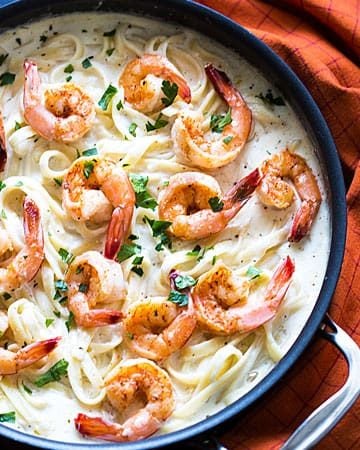 Overhead view of shrimp Alfredo in a skillet by a patterned napkin.