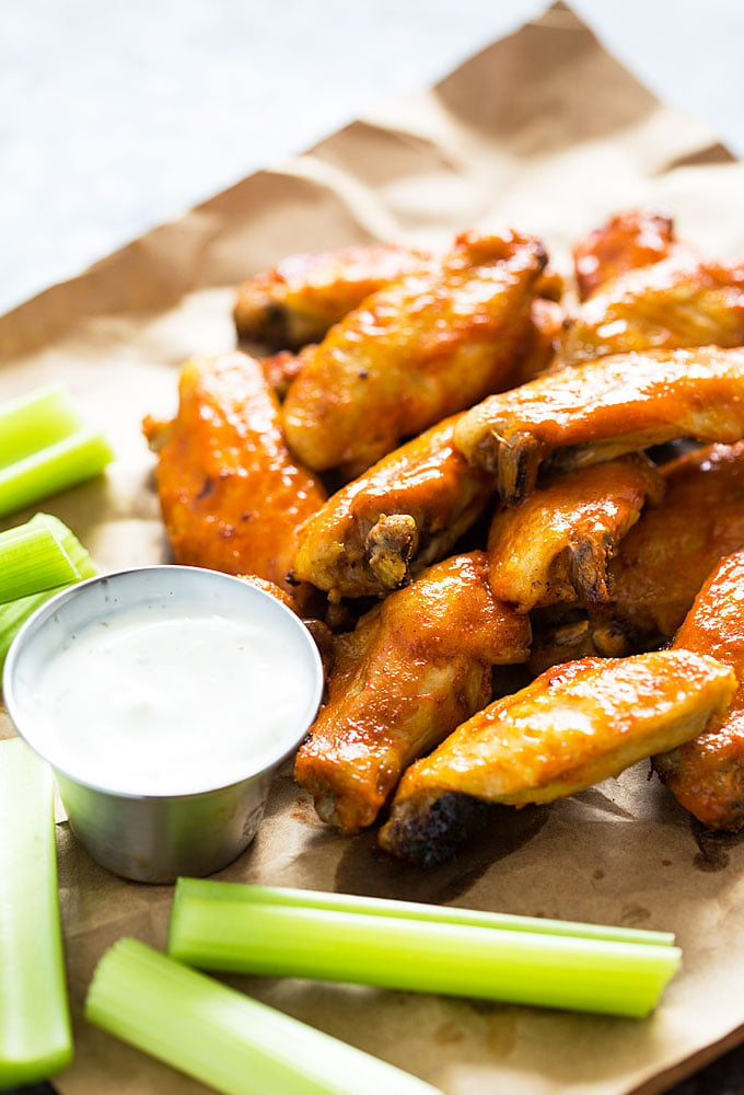 Chicken wings beside a cup of ranch dressing and celery sticks on brown paper.