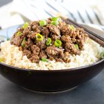 Front view of a gray bowl of rice topped with ground beef and sliced green onions.
