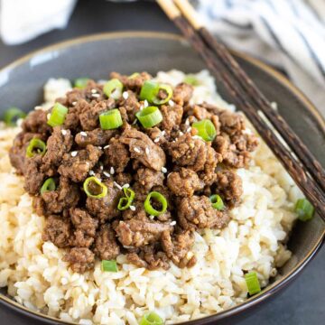 A bowl of rice topped with ground beef and green onions with a set of chopsticks.
