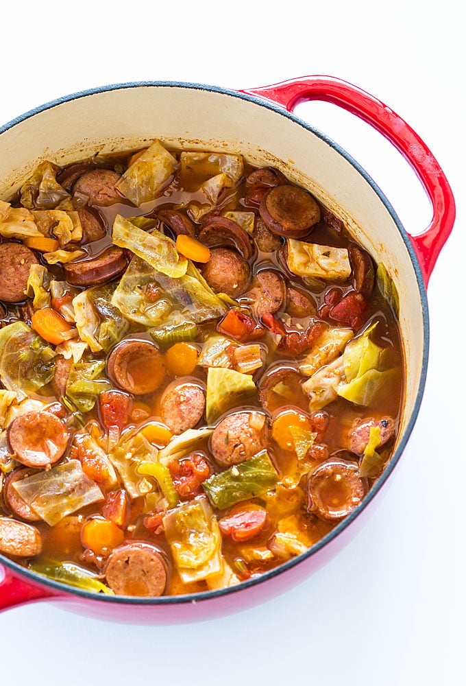 Overhead view of smoked sausage and cabbage soup in a red Dutch oven.