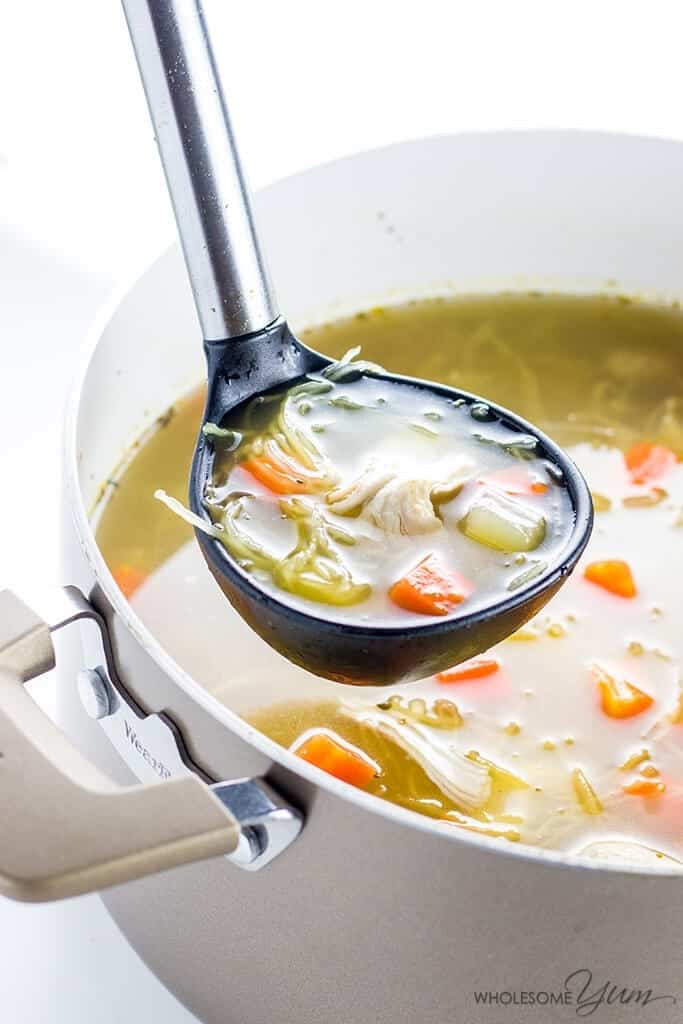 A ladle ladling chicken soup from a white pot.
