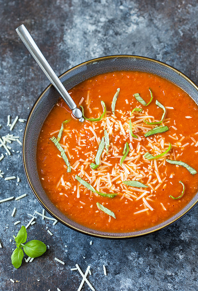 Overhead view of a gray bowl of tomato soup topped with grated Parmesan and basil.