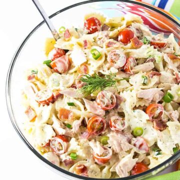Overhead view of a glass bowl of pasta salad with a spoon by a striped towel.