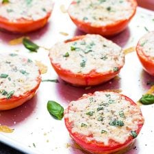 Baked Parmesan tomatoes topped with basil on a baking sheet.