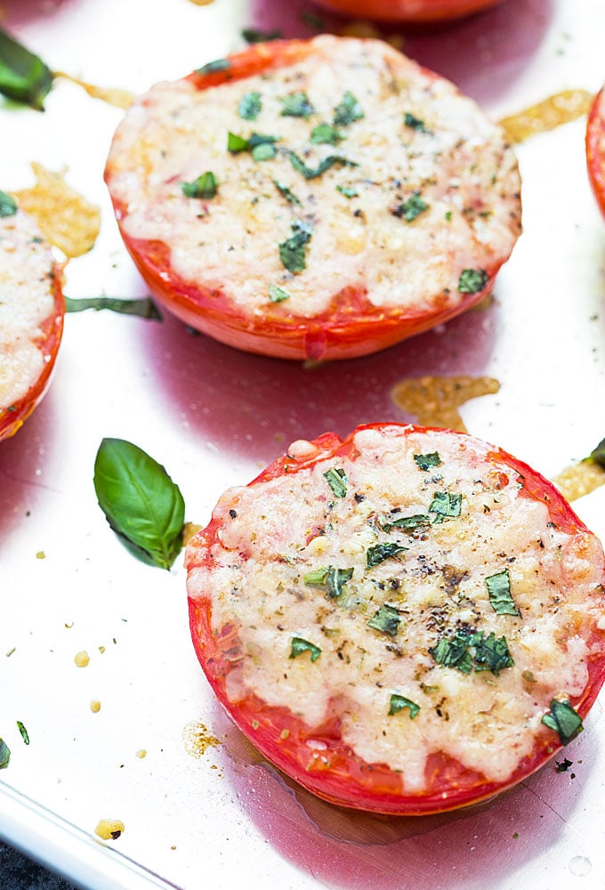 A close up of a baked tomato topped with melted cheese on a baking sheet.