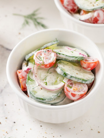Creamy cucumber tomato salad with onion in a white ramekin.