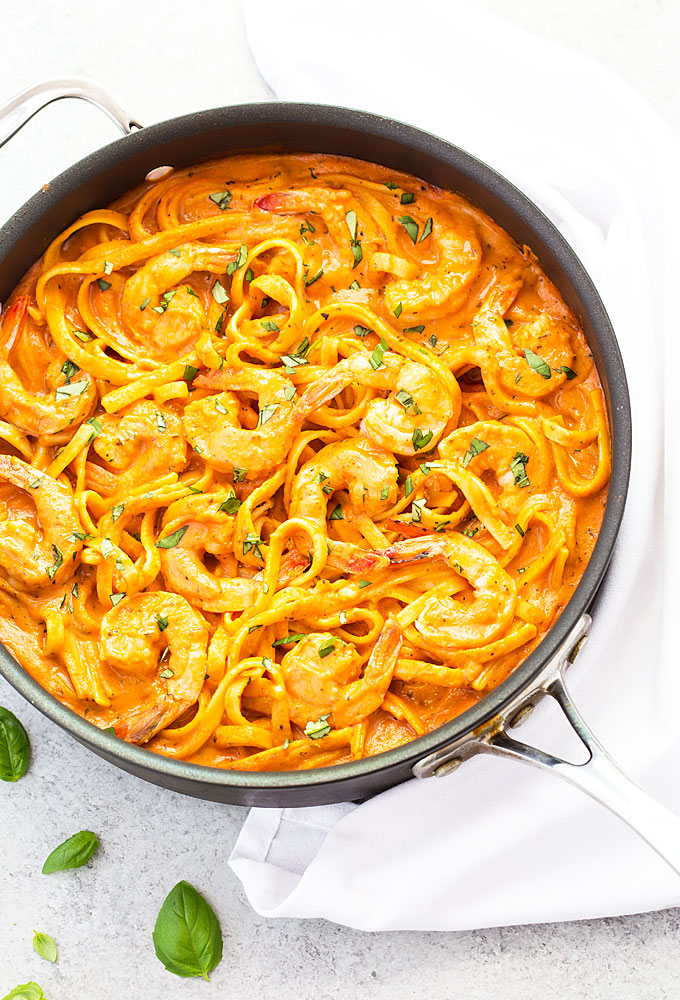 Overhead view of shrimp with fettuccine in a tomato cream sauce in a skillet.
