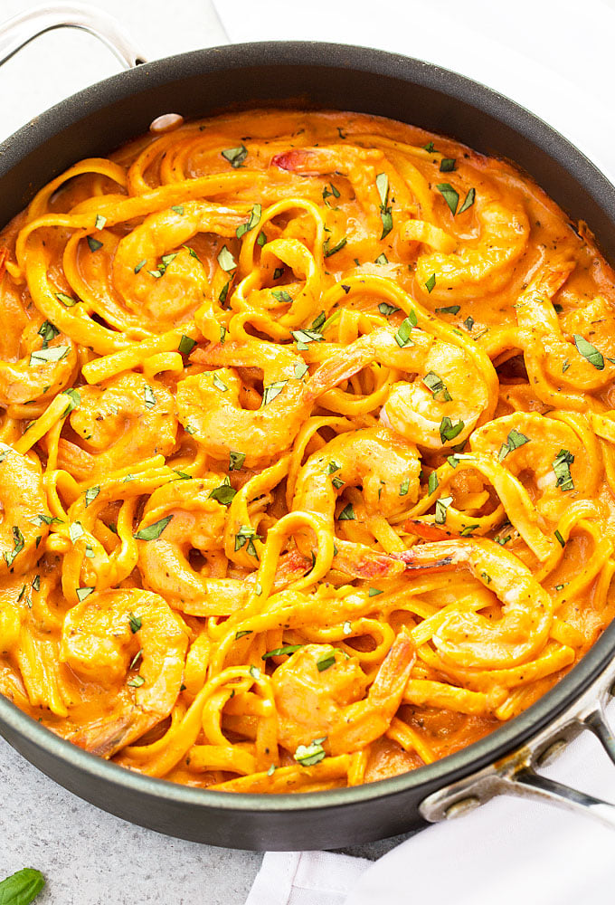 Closeup overhead view of shrimp with fettuccine and tomato cream sauce in a skillet.