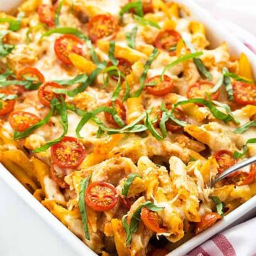 Chicken caprese pasta casserole topped with basil in a white baking dish.