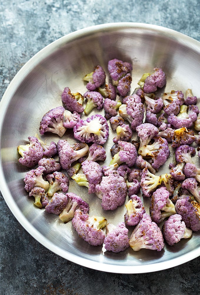 Overhead view of sauteed purple cauliflower florets in a stainless skillet.