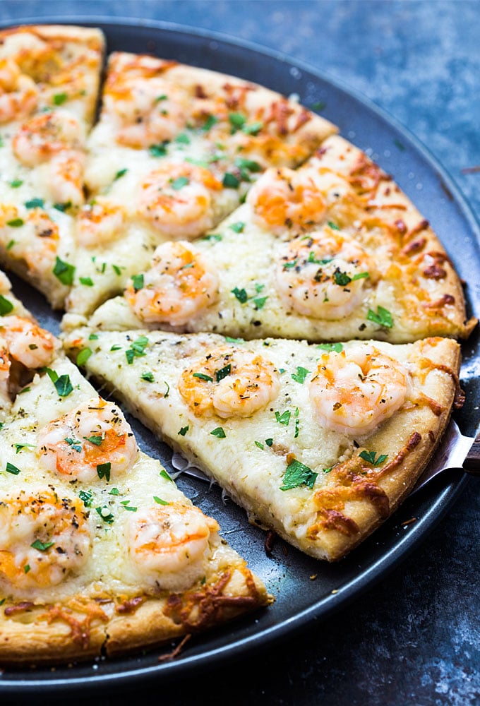 A closeup of a pizza server under a slice of shrimp scampi pizza on a pizza pan.