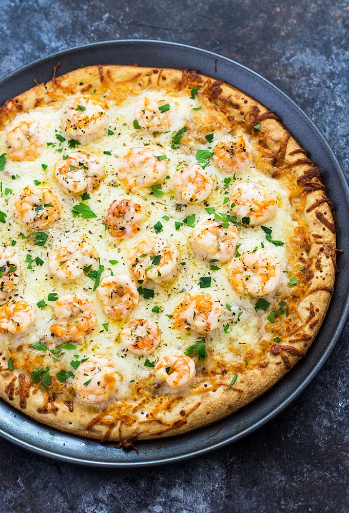 Overhead view of a shrimp pizza in a round on a dark surface.