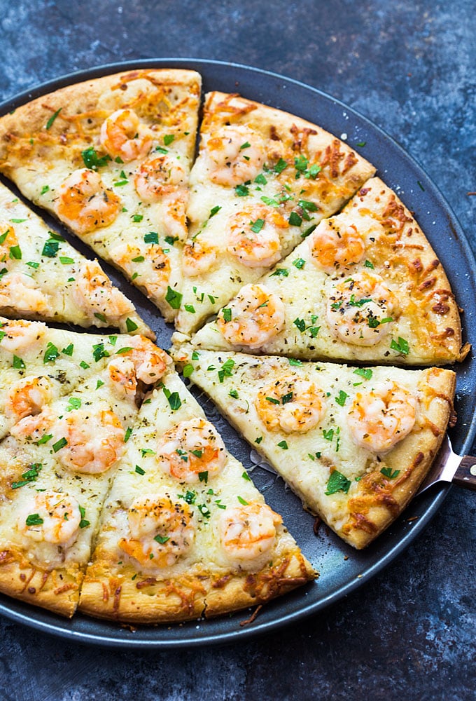 Overhead view of a sliced shrimp pizza on a round pan with a pizza server.
