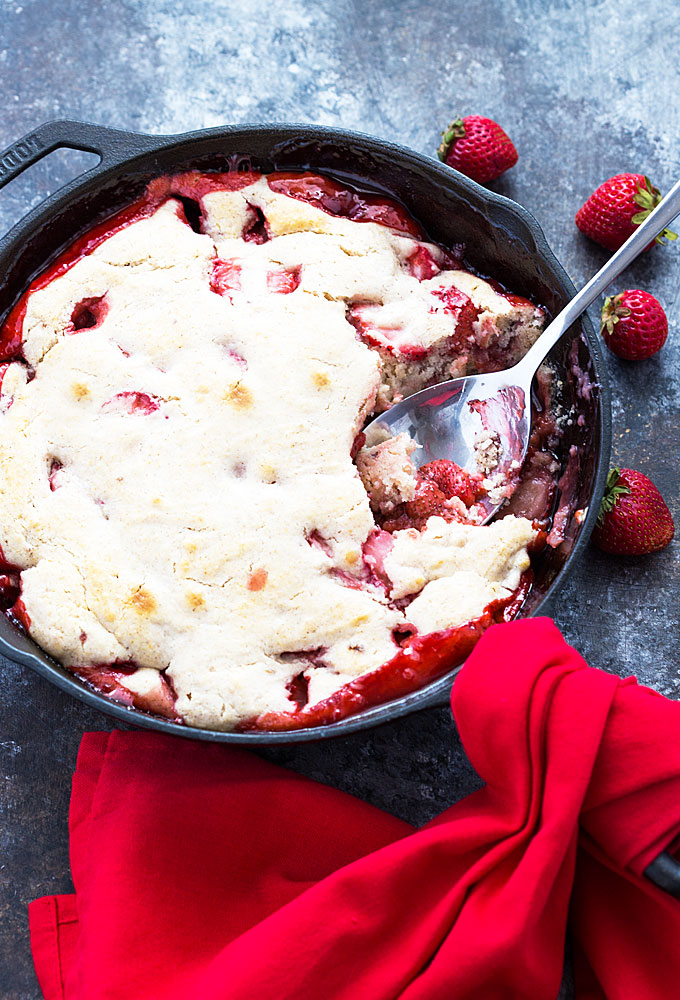 Overhead view of strawberry cobbler in a cast iron skillet with a spoon.