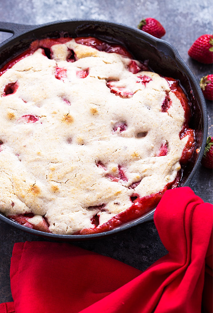 Strawberry cobbler in a cast iron skillet with a red towel wrapped around the handle.