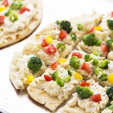 A closeup of flatbread topped with cheese spread and vegetables on a baking sheet.
