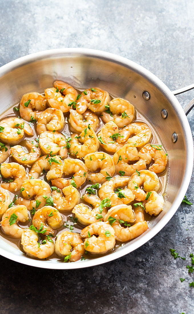 Honey garlic butter shrimp in a stainless skillet on a dark surface.