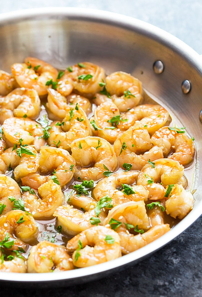 A closeup view of shrimp in a honey sauce topped with parsley in a skillet.