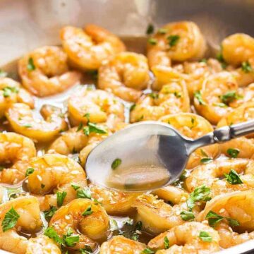 A spoon spooning a honey garlic butter sauce over shrimp in a skillet.