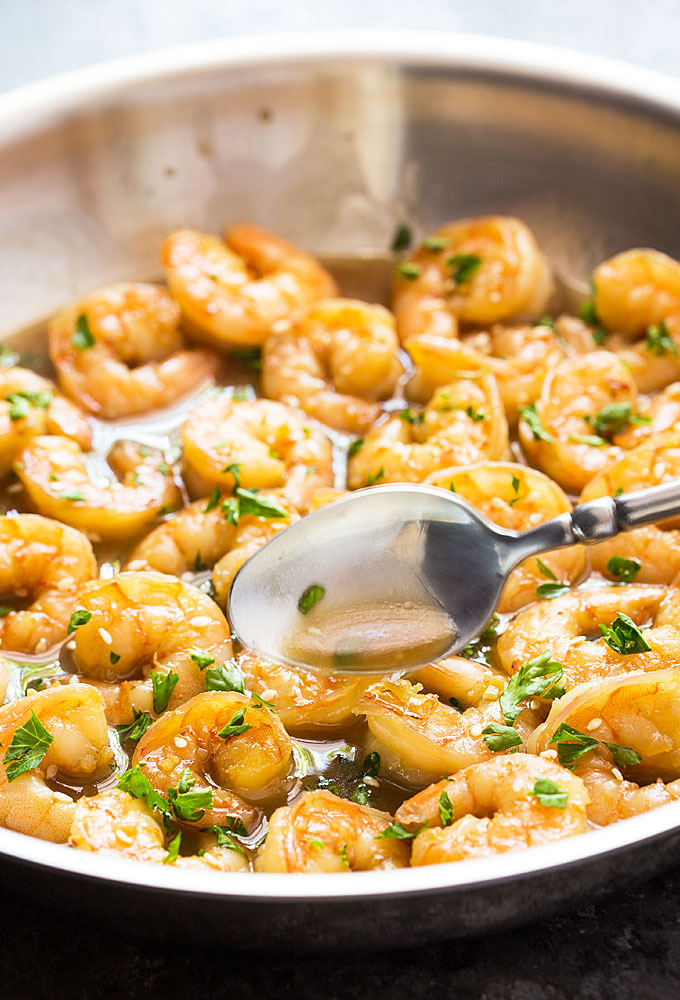 A spoon spooning a garlic honey butter sauce over shrimp in a skillet.