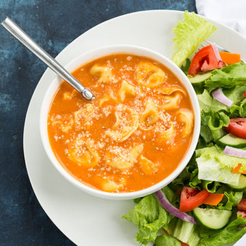 Overhead view of tomato tortellini soup in a white bowl.